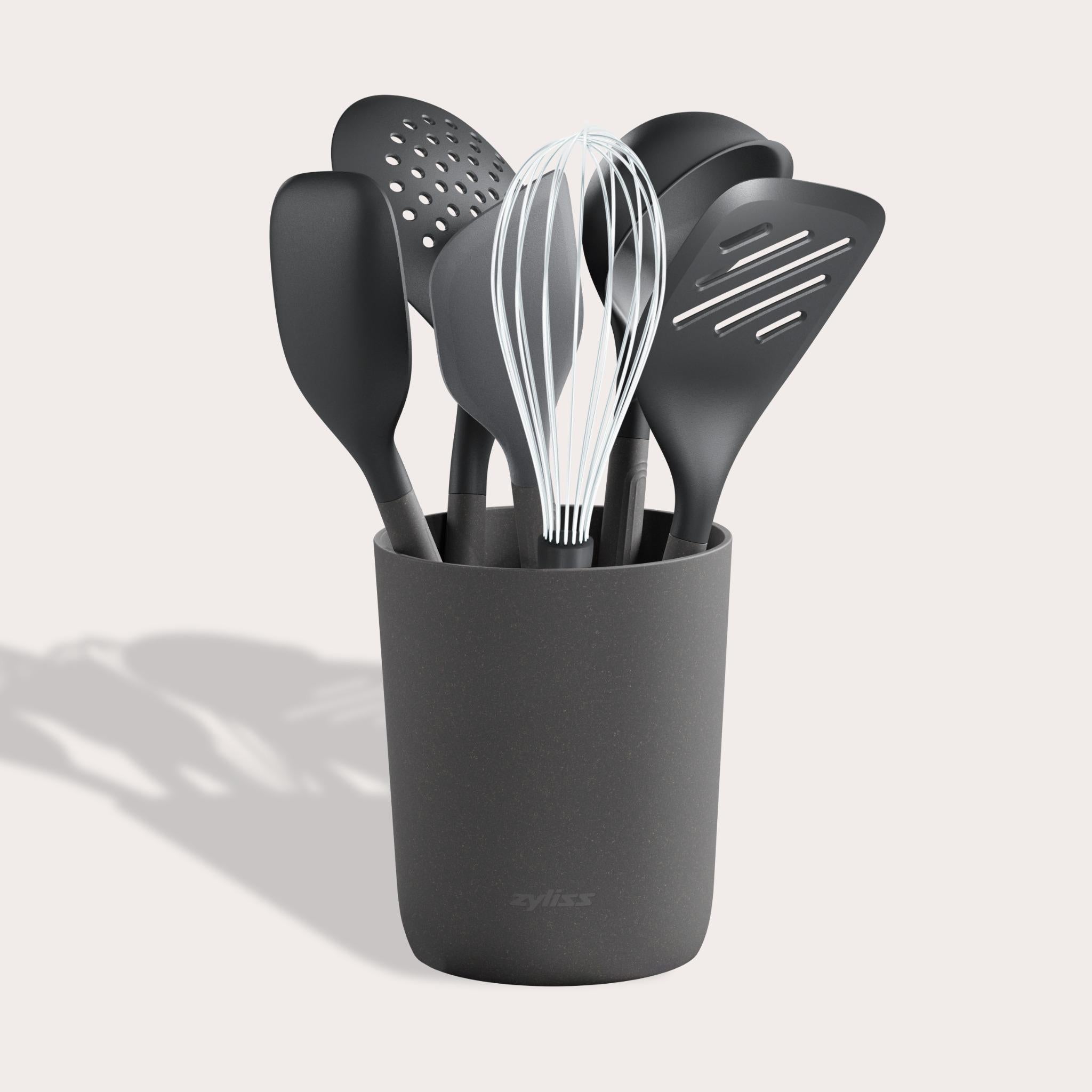 The Zyliss 7-Piece Utensil Set includes black kitchen tools—whisk, spatulas, spoon, and slotted spoon—organized in a matching container. Each features ergonomic handles and heat-resistant PBT for safe, comfortable use.
