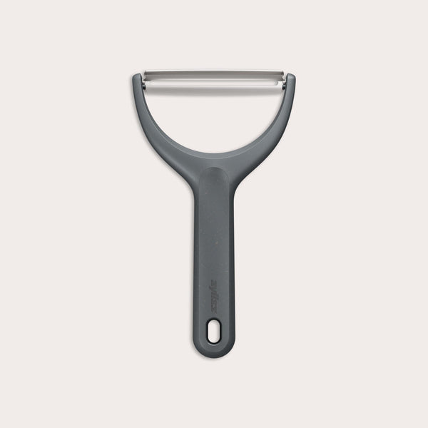 The Zyliss Wide Peeler features a Y-shaped design, ergonomic handle, and horizontal stainless steel blade, shown against a simple light background. 