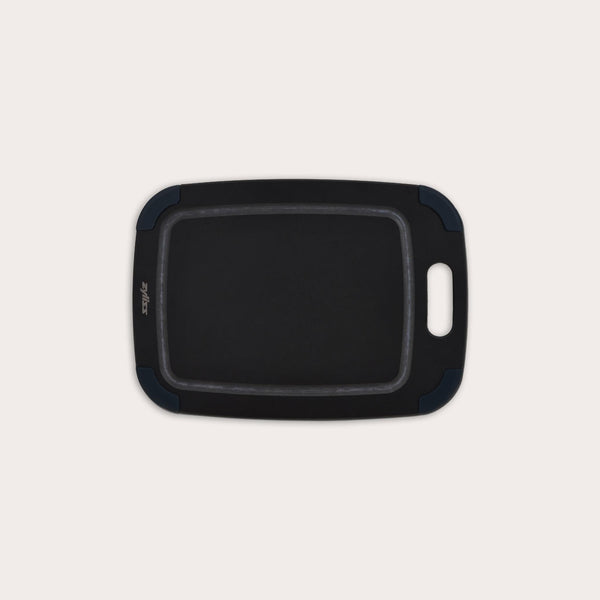 The Zyliss Wood Fibre Cutting Board is rectangular with rounded edges, a built-in handle, and dark blue corner grips. Made from recycled wood fibres, it is shown on a plain light background. #Small