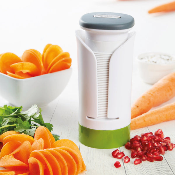 The Zyliss Spiralizer sits on a white table with spiral-cut carrots, a bowl of cilantro, pomegranate seeds, and a dip in the background. Sliced spiral carrots are decoratively arranged around the durable Zyliss Spiralizer.