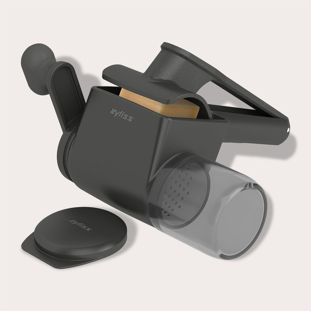 The Zyliss Professional Rotary Cheese Grater Set, in black, features an ergonomic crank, transparent detachable container, and visible grater drum with the handle extended.