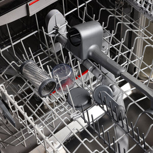 A Zyliss Professional Rotary Cheese Grater Set with detachable container and ergonomic crank, along with other gray and clear kitchen tools, sits on the top rack of an open dishwasher, ready for cleaning.