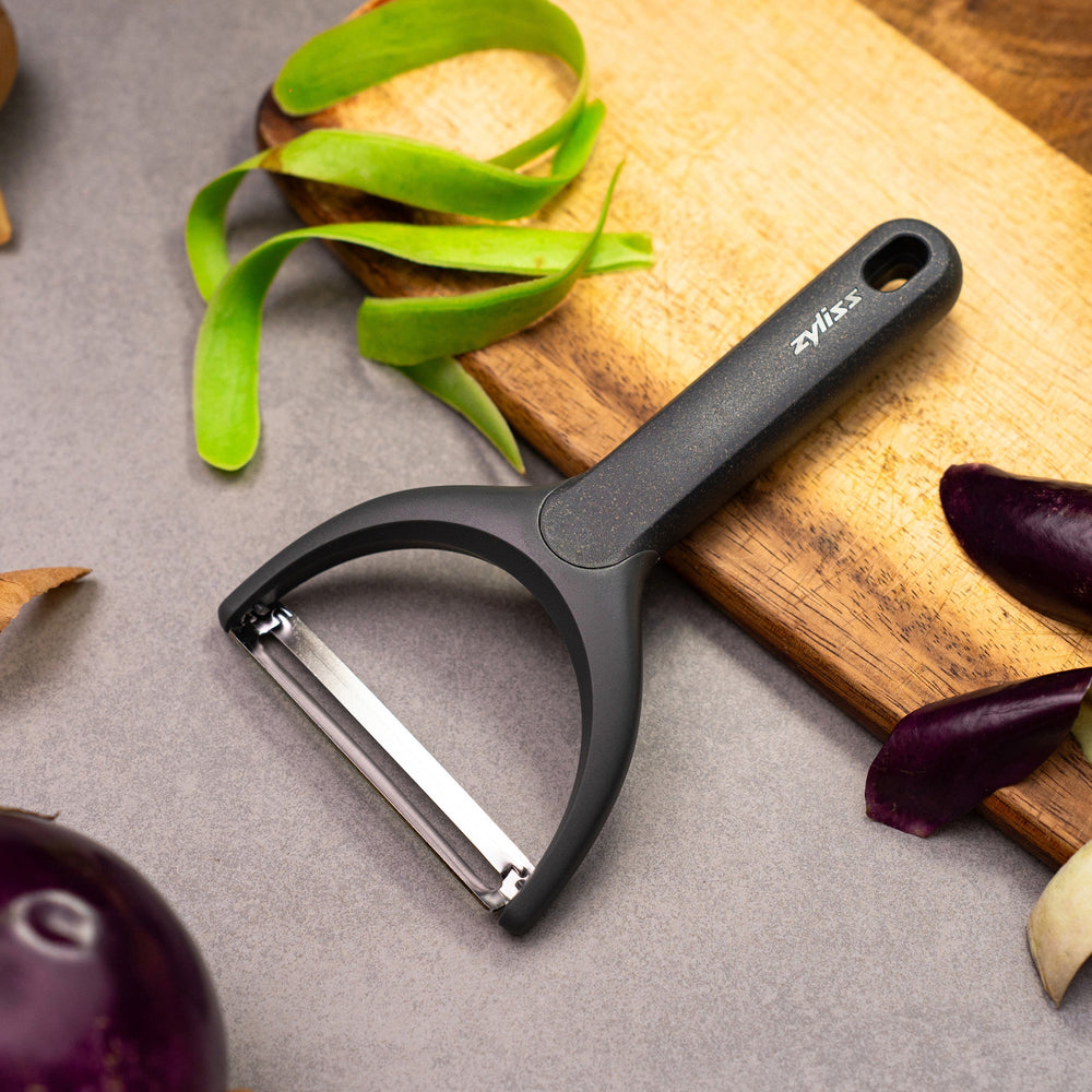 The Zyliss Wide Peeler features a Y-shaped design, ergonomic handle, and horizontal stainless steel blade, shown against a simple light background. 