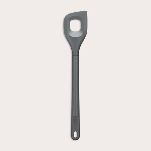 The Zyliss Angled Mixing Spoon is a gray silicone utensil with an ergonomic handle and a rectangular hole in the head, designed for non-stick cookware. Shown on a plain white background.