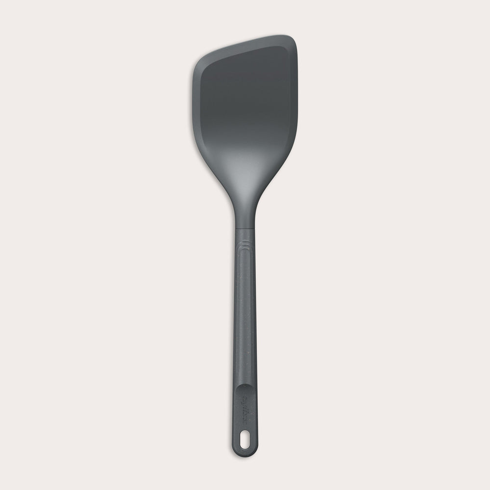 The Zyliss Angled Turner is a dark gray, heat-resistant silicone utensil with a slightly angled rectangular head and long handle, shown on a plain light background. Safe for use on non-stick surfaces.