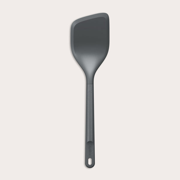 The Zyliss Angled Turner is a dark gray, heat-resistant silicone utensil with a slightly angled rectangular head and long handle, shown on a plain light background. Safe for use on non-stick surfaces.