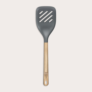 The Zyliss Oak Wood Slotted Turner is a kitchen essential with a wide, dark gray head and light oak wood handle, shown on a plain white background.