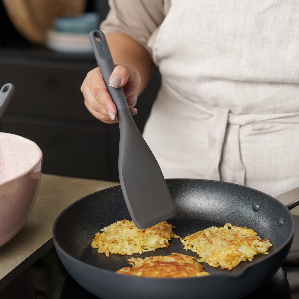 The Zyliss Easy Lift Turner is a gray, heat-resistant silicone utensil with a rectangular, angled head and long handle with hanging hole—perfect for non-stick cookware. Shown on a plain white background.
