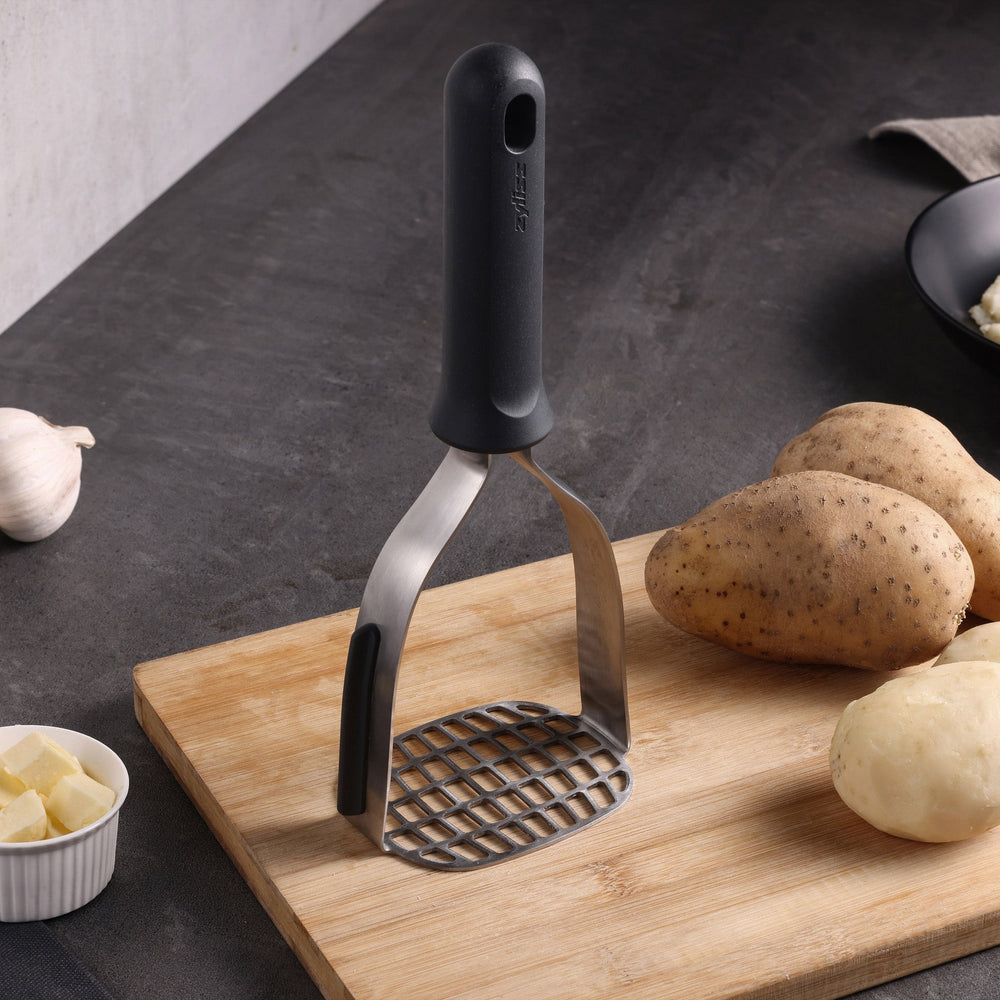 The Zyliss Potato Masher is a gray kitchen tool with a wide, flat stainless steel head and sturdy handle. Its designed for mashing potatoes or other foods, and the handle has a hole at the top for easy hanging.