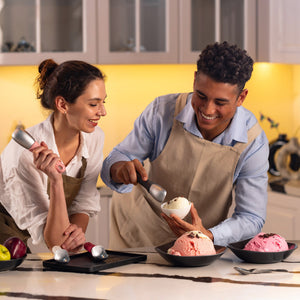 #belugagrey A man and woman in aprons smile as they use the Zyliss Ice Cream Scoop, featuring a sustainable wheat straw, eco-friendly handle, to serve various flavors into bowls on the counter.