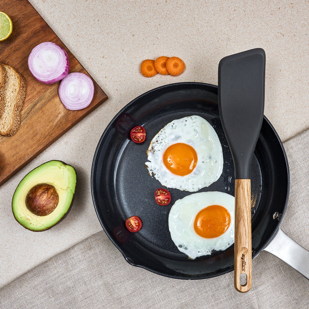 The Zyliss Oak Wood Easy Lift Turner has a dark gray silicone head, an oak wood handle, and a hanging hole at the end. It is shown on a plain light background.