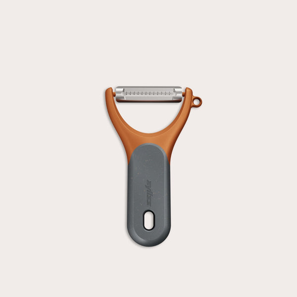 The Zyliss Julienne Y Peeler features an orange handle, gray ergonomic grip, and a horizontal stainless steel blade, displayed on a plain white background.