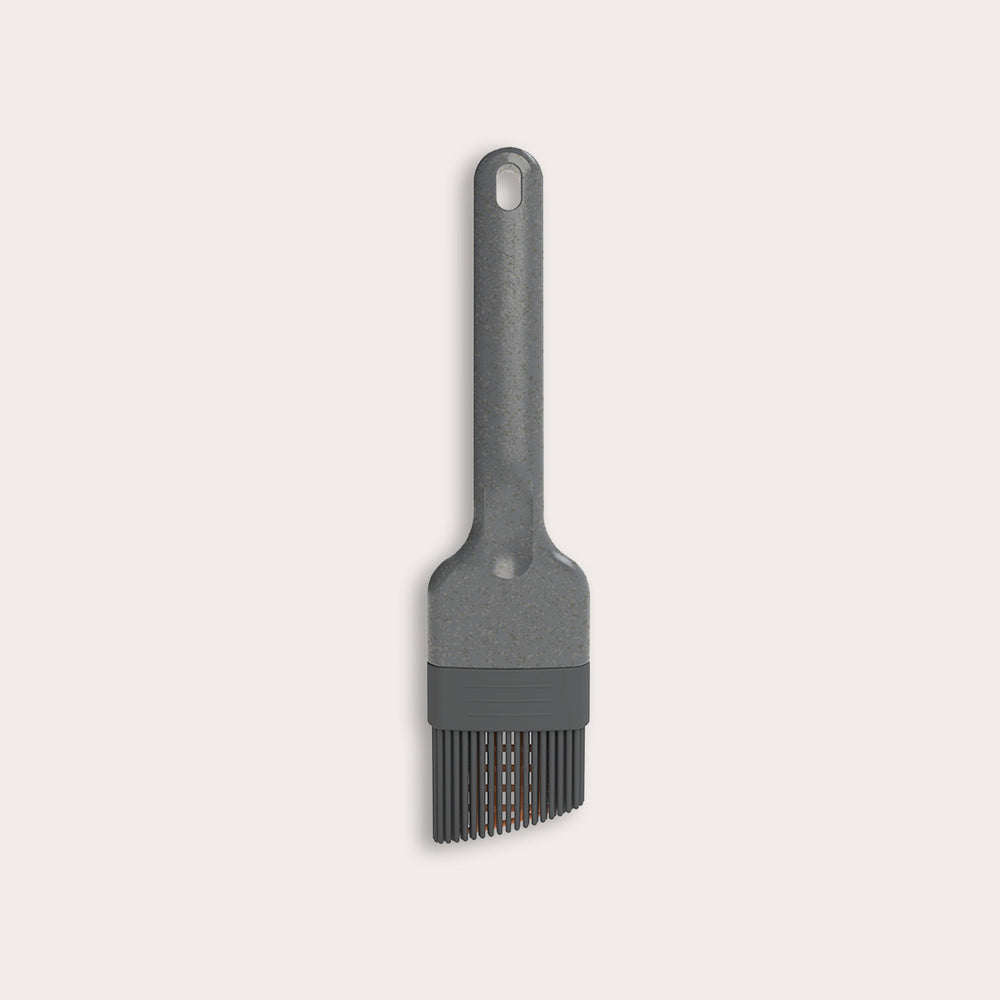 The Zyliss Silicone Pastry Brush is gray, heat-resistant, and dishwasher safe. It features a long handle with a hanging hole and flexible bristles ideal for spreading sauces or oils. Shown against a plain, light-colored background.