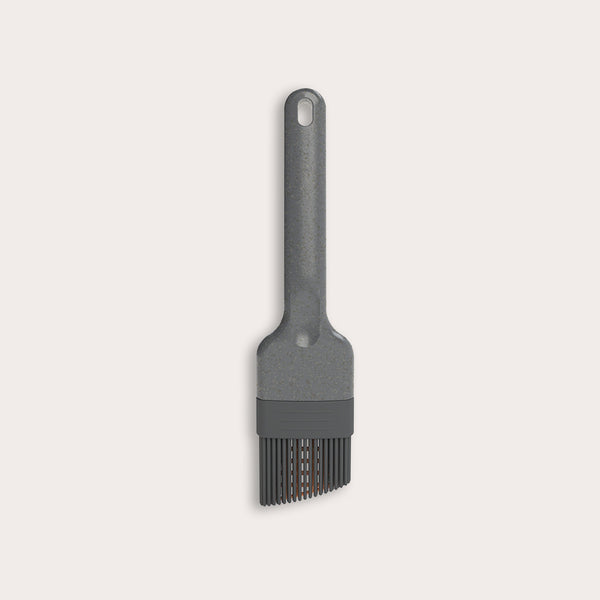 The Zyliss Silicone Pastry Brush is gray, heat-resistant, and dishwasher safe. It features a long handle with a hanging hole and flexible bristles ideal for spreading sauces or oils. Shown against a plain, light-colored background.