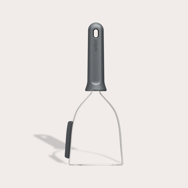 The Zyliss Potato Masher is a gray kitchen tool with a wide, flat stainless steel head and sturdy handle. Its designed for mashing potatoes or other foods, and the handle has a hole at the top for easy hanging.