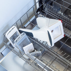 A disassembled white and black kitchen tool with several grater attachments is placed on the top rack of an open dishwasher.