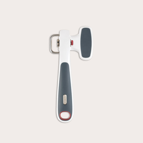 The Zyliss Safe Edge Can Opener has an ergonomic design, white and dark gray handle with red accents, and a metal turning mechanism, displayed against a plain light background.